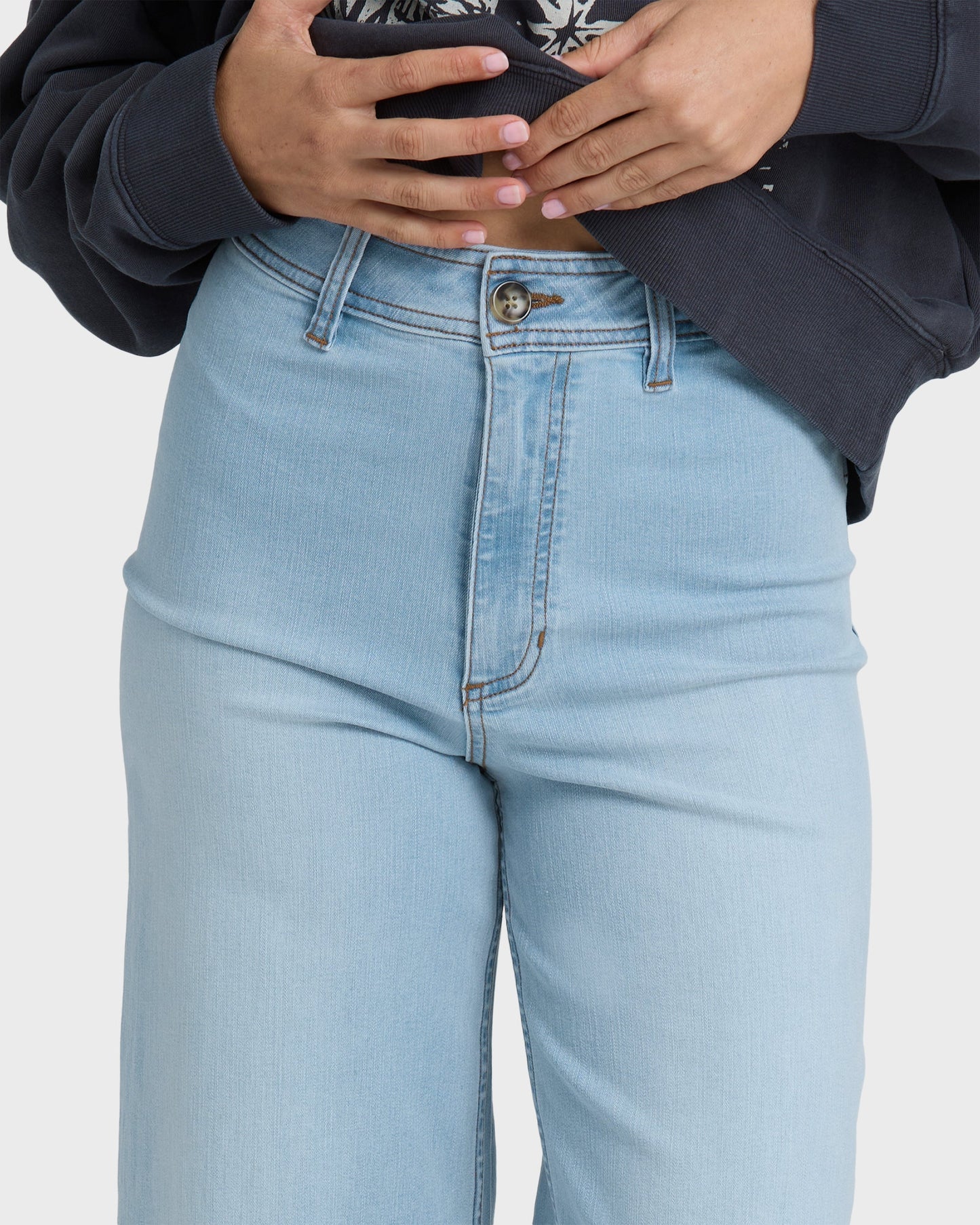 Light blue high-waist denim pants with button fly and visible seaming, worn with black jacket.