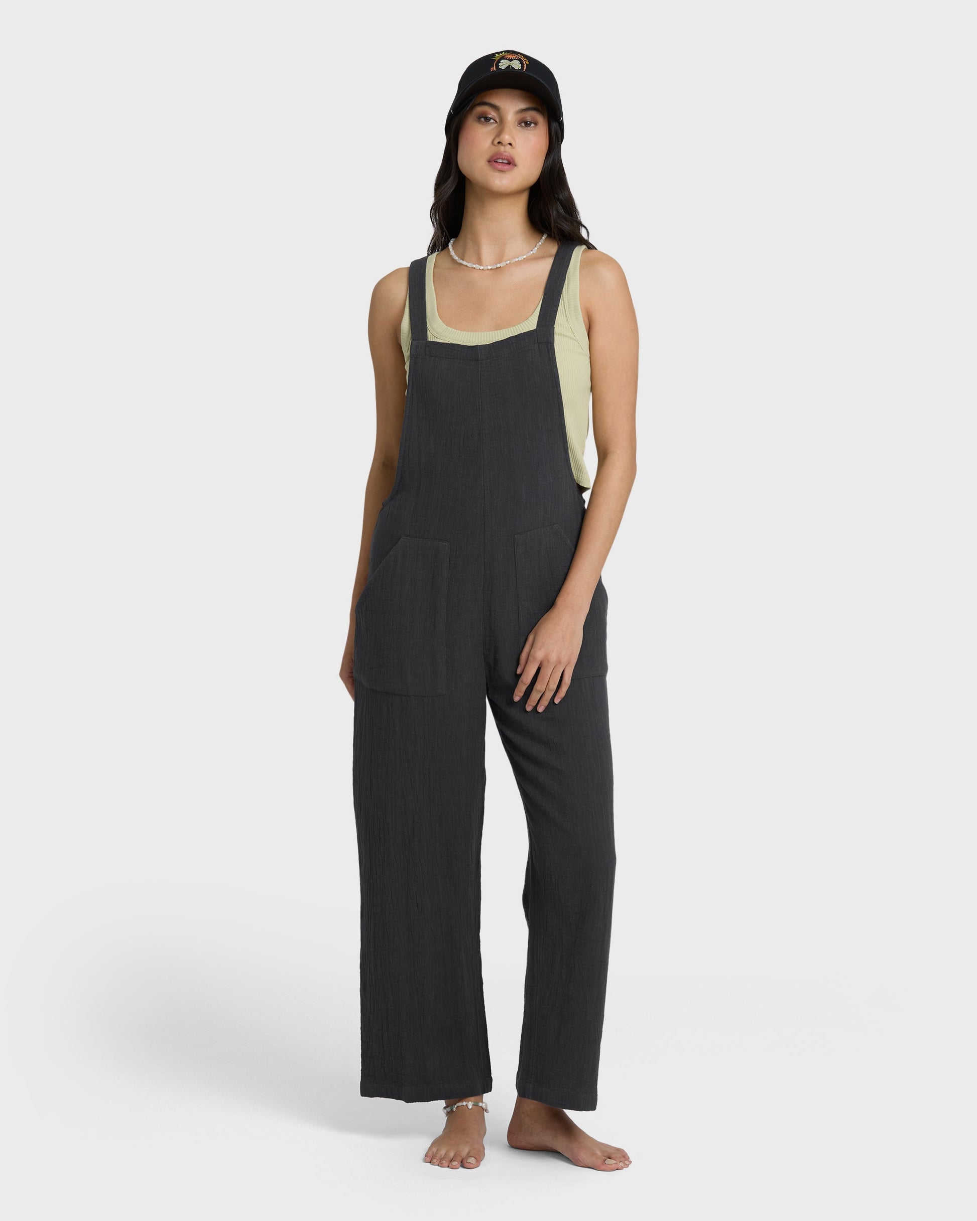 Black sleeveless jumpsuit with square neckline and wide-leg pants, worn with sage green tank layered underneath.