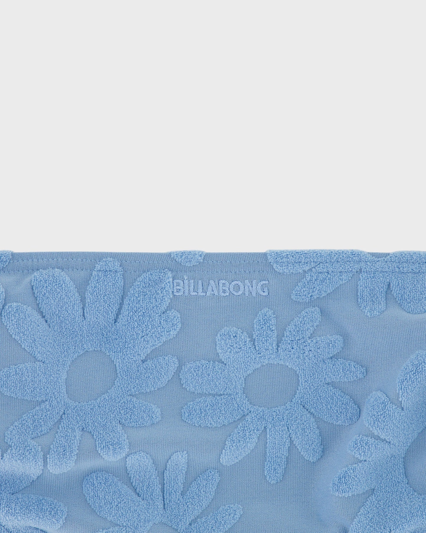 Blue towel with floral patterns and 'Billabong' branding on a light gray background