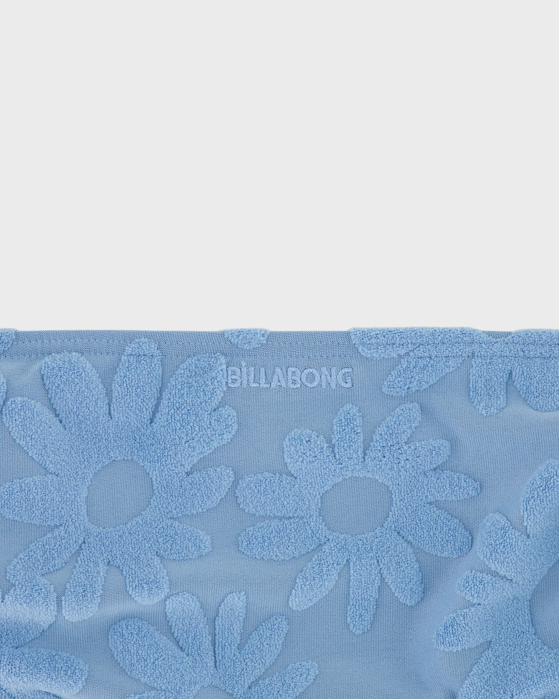 Blue towel with floral patterns and 'Billabong' branding on a light gray background