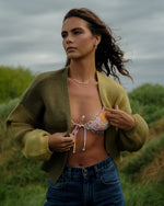 Woman wearing an open green tea-colored knit cardigan with ribbed cuffs over a bikini top and denim jeans.