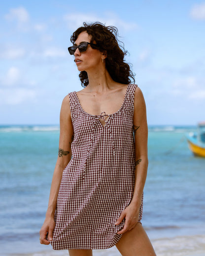 Red and white gingham sleeveless dress with front tie detail on a woman at the beach.