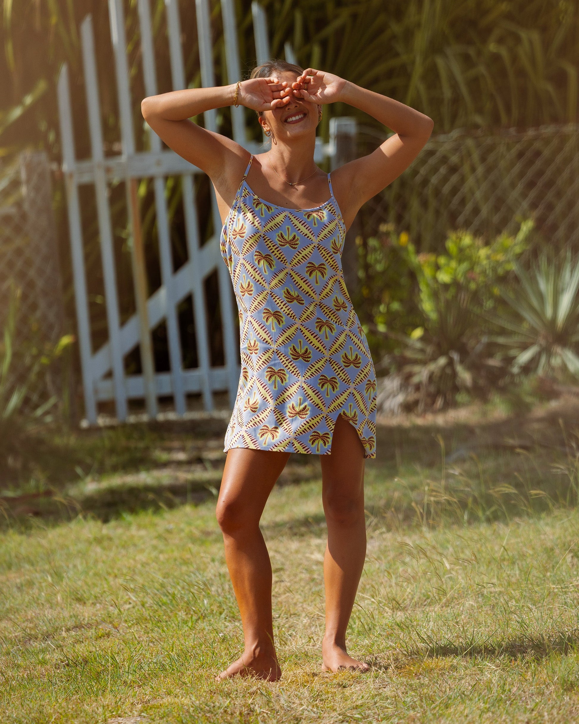 Sleeveless sundress with blue background and yellow palm tree print, thin straps, knee-length.