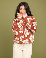 Rust-colored sherpa half zip sweatshirt with cream floral pattern, worn with cream pants.