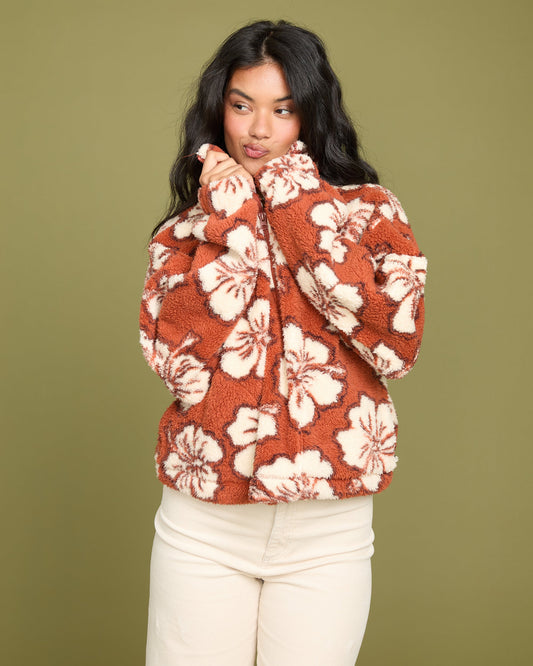 Rust-colored sherpa half zip sweatshirt with cream floral pattern, worn with cream pants.
